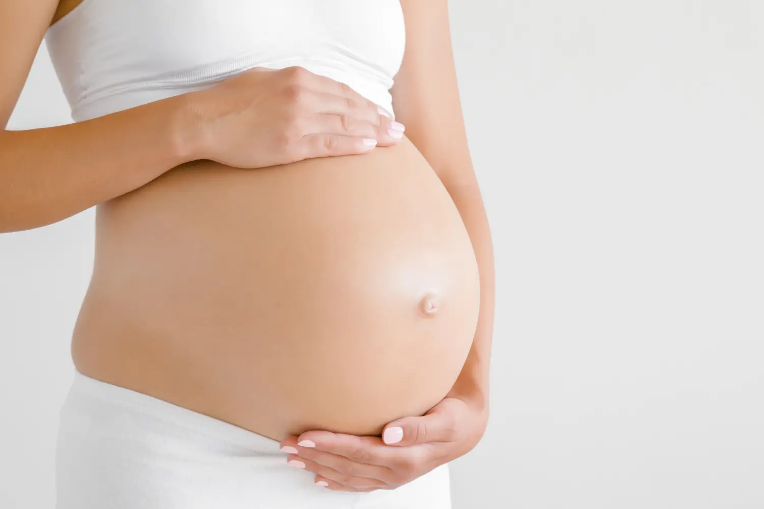 Frau steht und berührt mit den Händen ihren nackten dicken Bauch. Isoliert auf grauem Hintergrund.